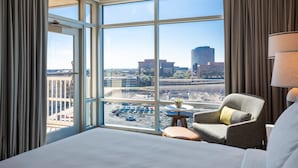 Une chambre d’hôtel dotée d’une grande fenêtre donnant sur la ville, d’un lit, d’une chaise et d’une petite table sur laquelle est posée une plante.