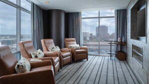 Une chambre d’hôtel moderne dotée d’une grande fenêtre, d’un téléviseur à écran plat et d’un coin salon avec des fauteuils en cuir et un tapis à rayures.