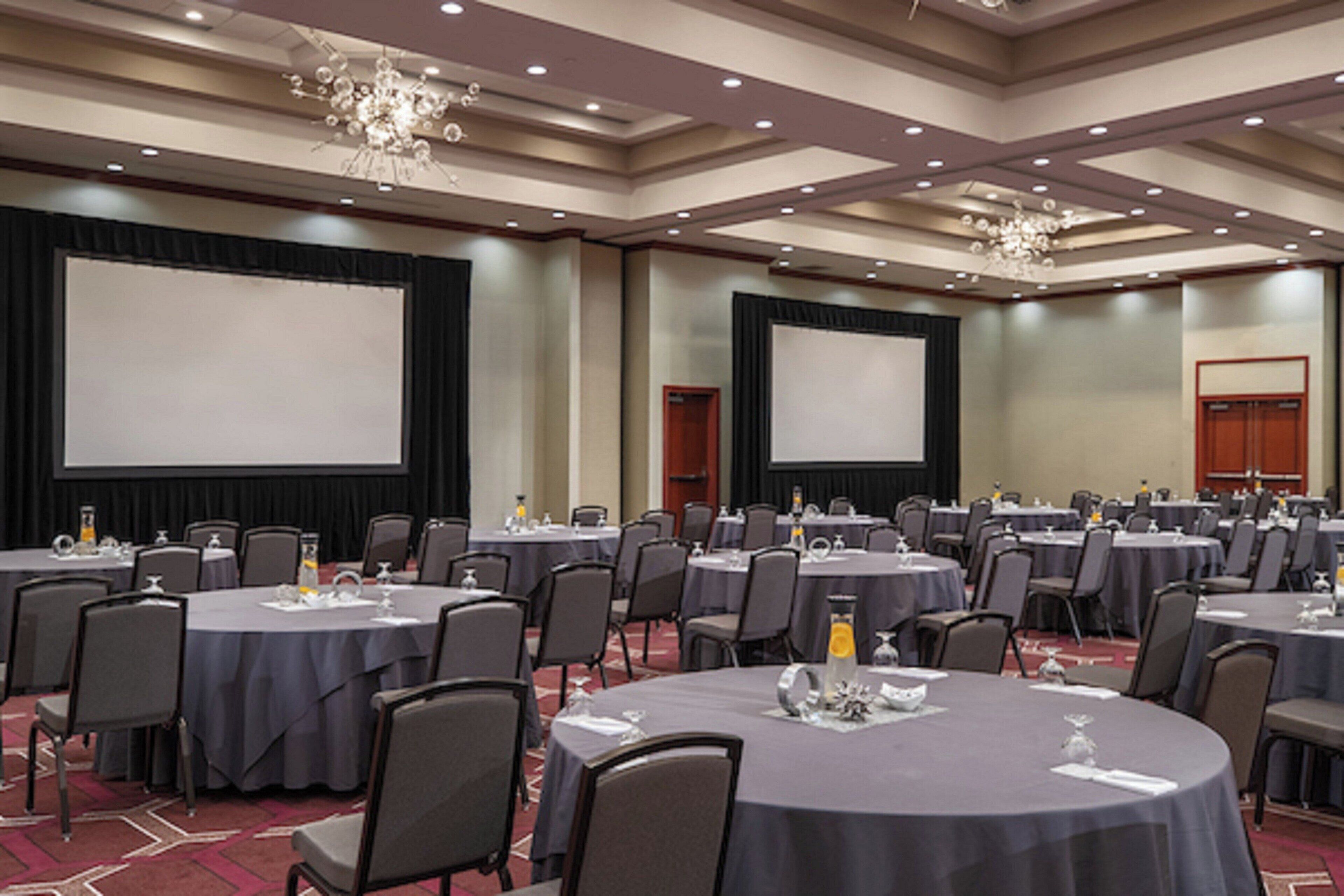 A conference room with multiple round tables, chairs, and a large screen.