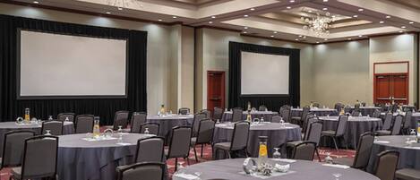 A conference room with multiple round tables, chairs, and a large screen.