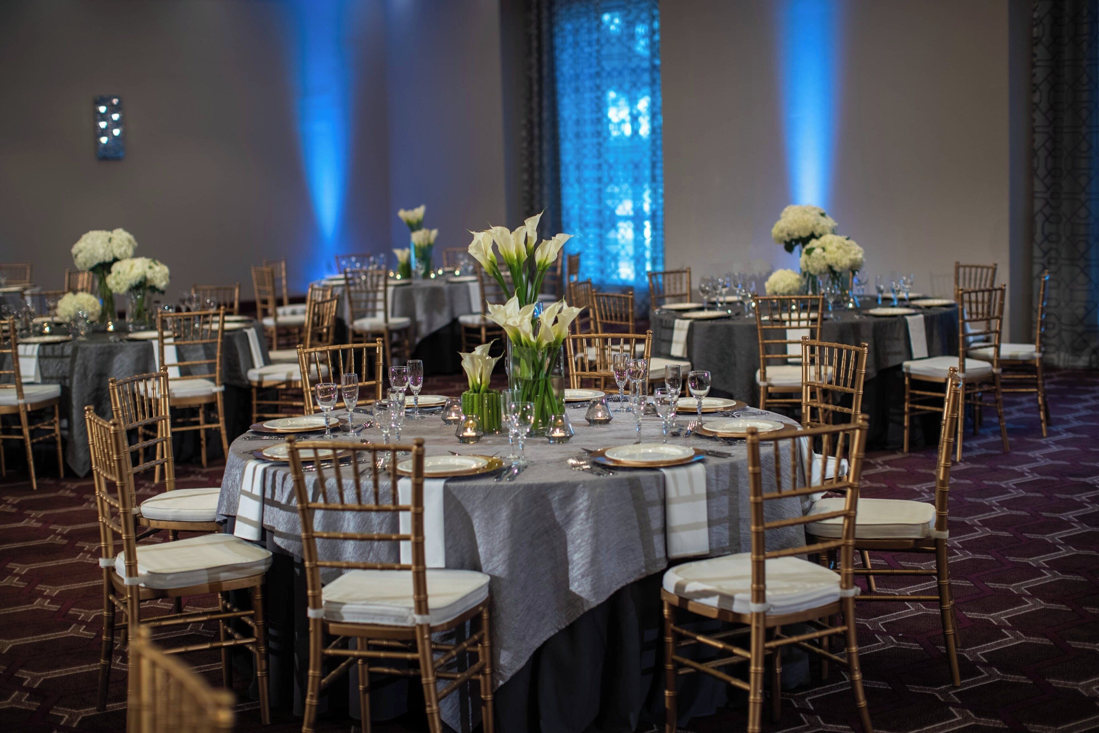 A banquet hall with round tables, gold chairs, and white flowers.