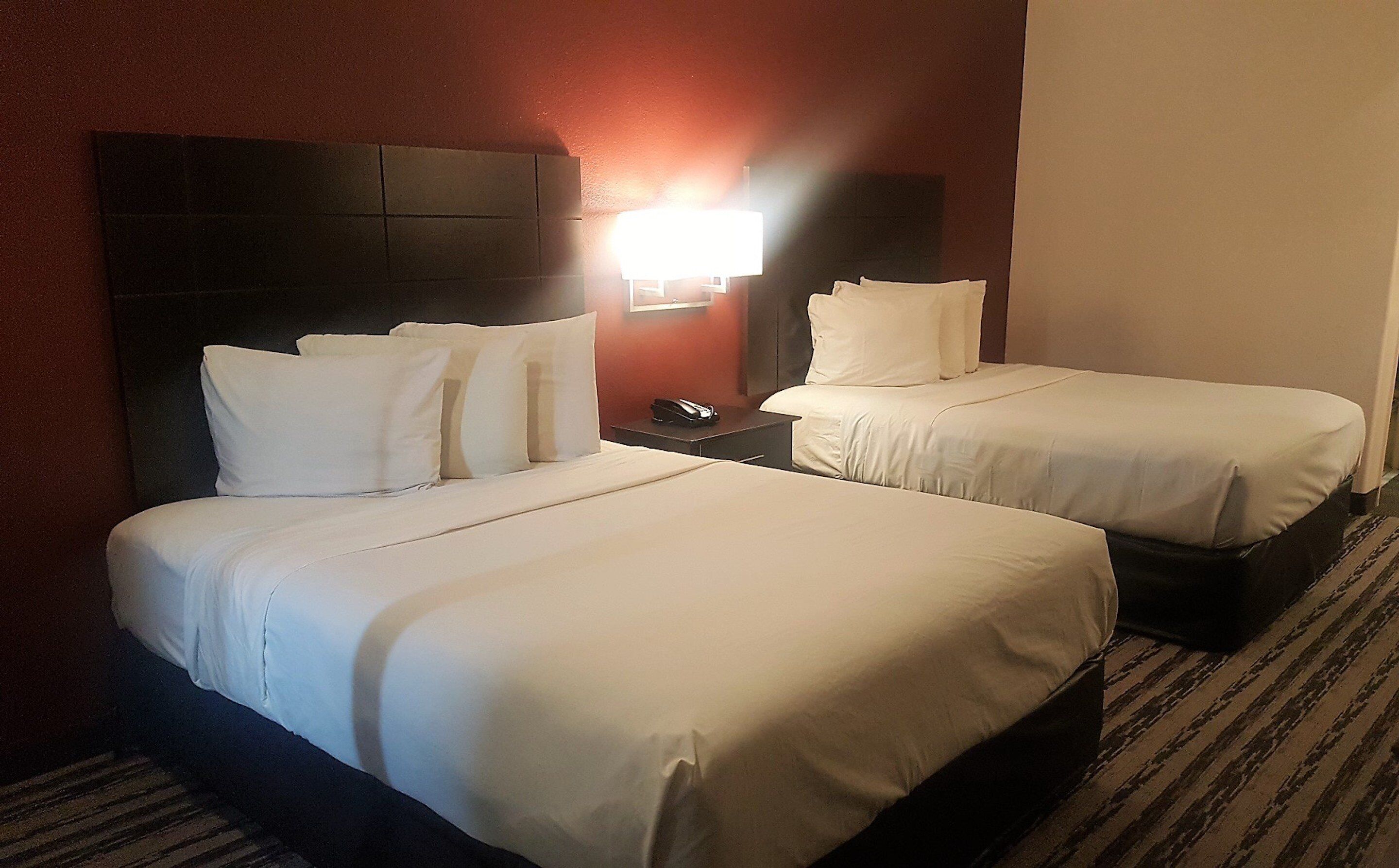 A hotel room with two beds, a nightstand, and a wall-mounted lamp.