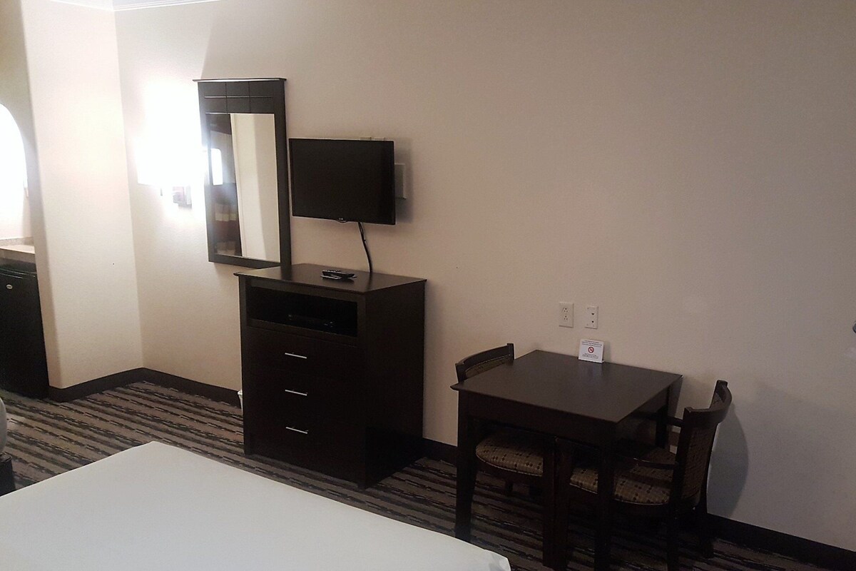 A hotel room with a bed, a desk, a chair, a dresser, a television, and a mirror.