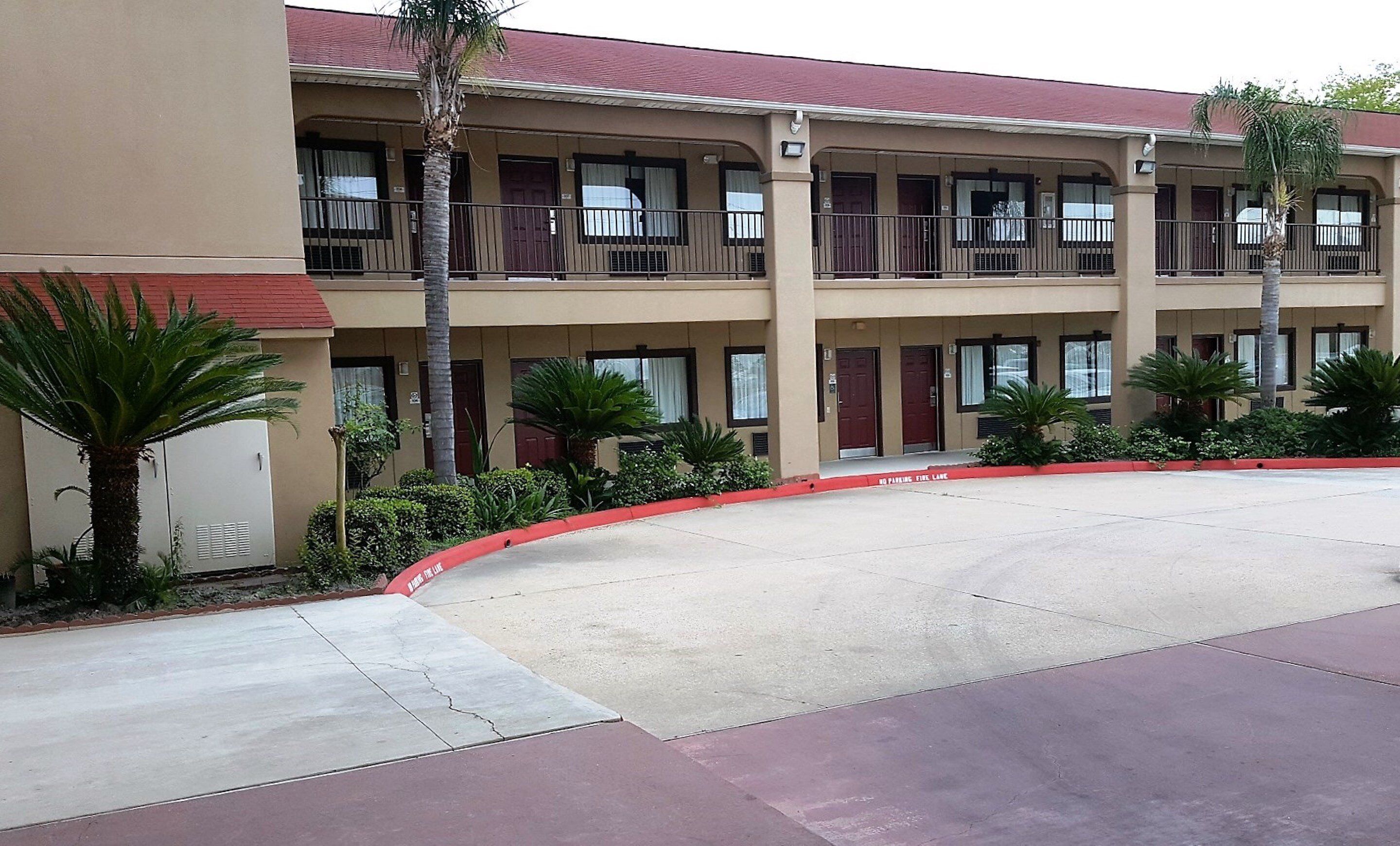 A multi-story motel with balconies, a parking lot, and palm trees.