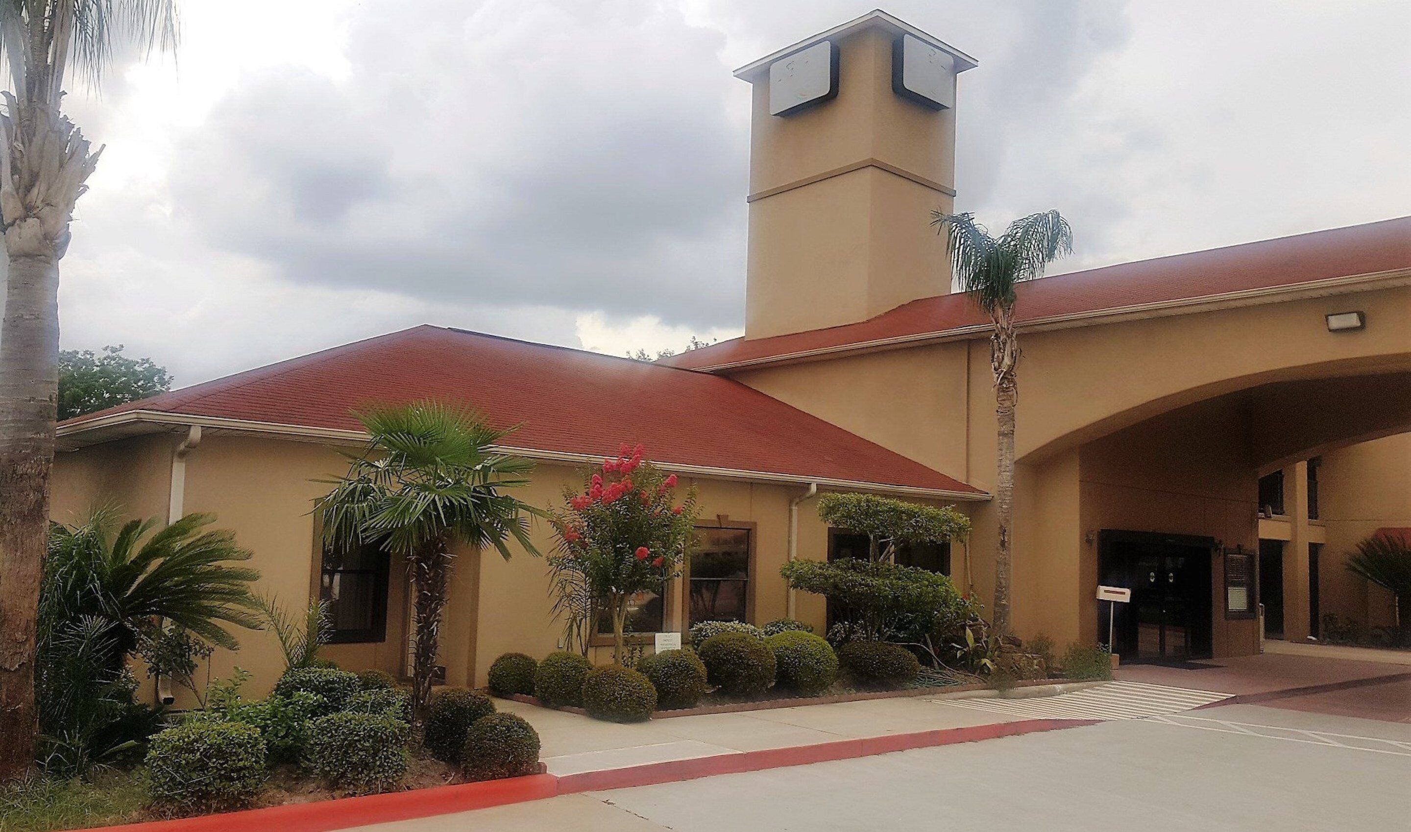 A building with a red roof and beige walls, featuring a tower and an entrance with a canopy.