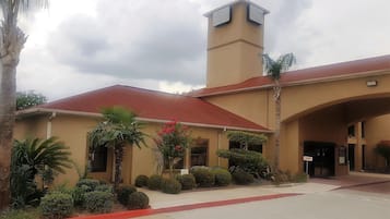 A building with a red roof and beige walls, featuring a tower and an entrance with a canopy.