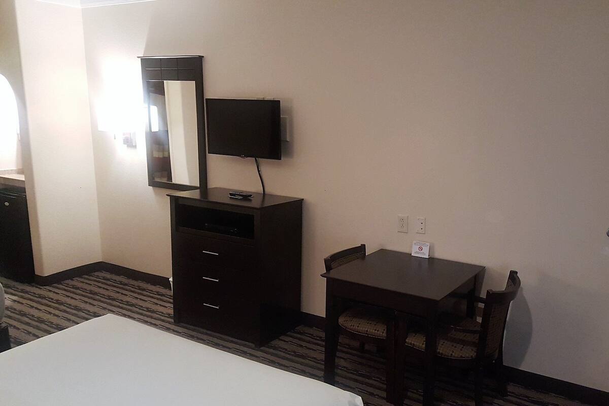 Une chambre d’hôtel comprenant un lit, un bureau avec une chaise, une commode, un téléviseur posé sur la commode et un miroir.