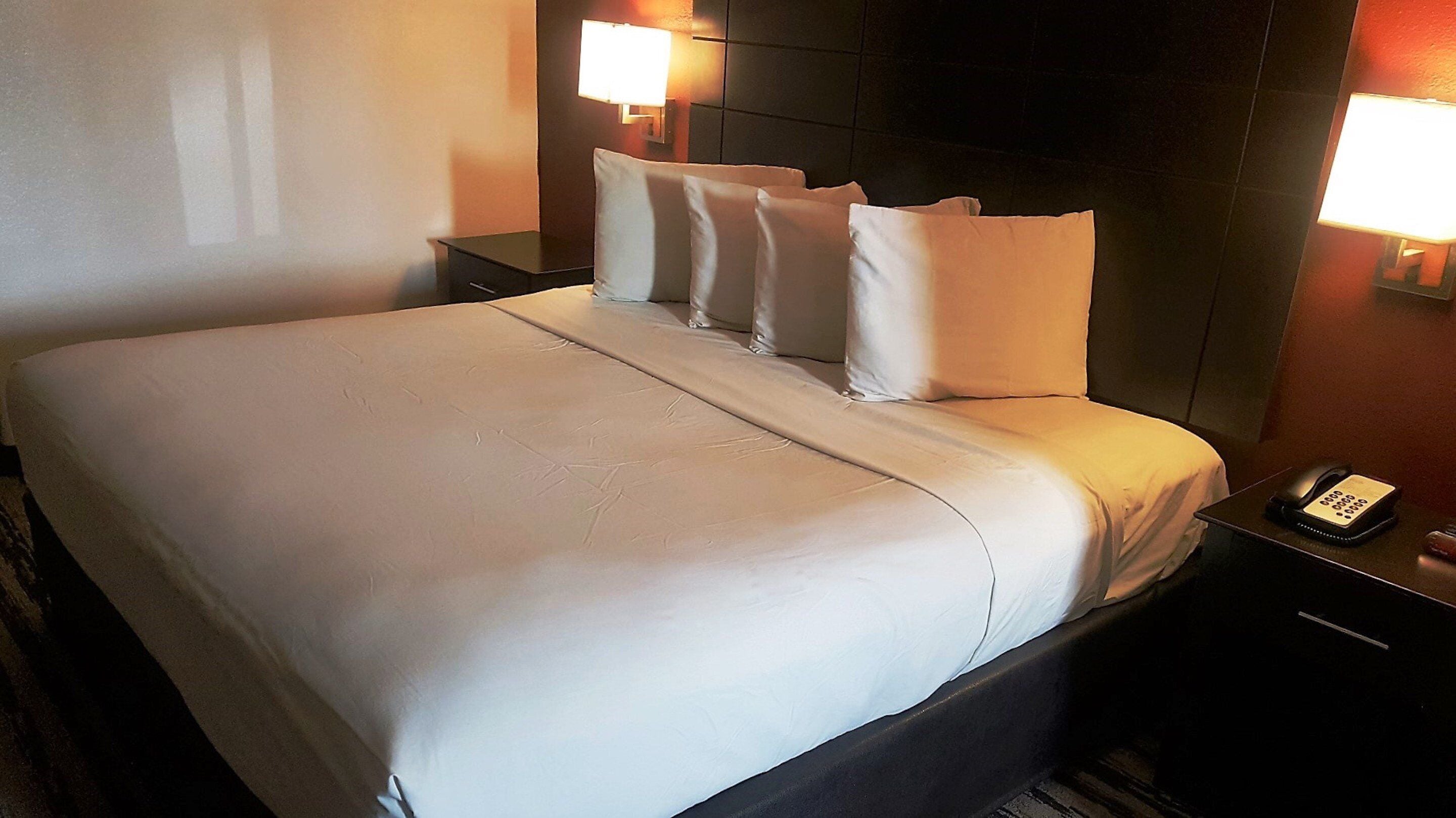 Habitación de hotel con una cama grande, dos mesitas de noche, un teléfono y lámparas de pared.