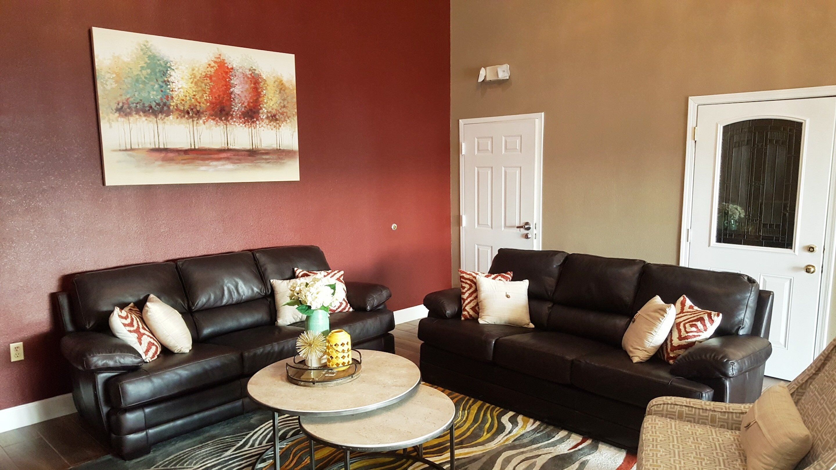 A living room with two black leather sofas, a round coffee table, and a painting on the wall.