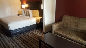 Hotellihuone, jossa on sänky, yöpöytä, lamppu, sohva ja pieni pöytä.
