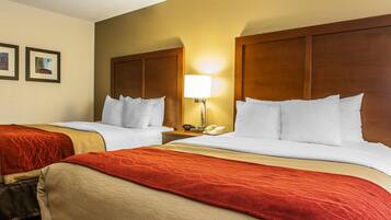 A hotel room with two beds, a nightstand with a lamp, and framed pictures on the wall.