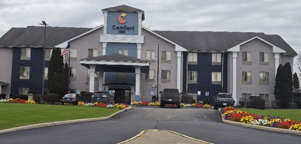 A Comfort Inn hotel with a central entrance, multiple parking spaces, and a well-maintained flower bed in front.