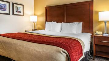 A hotel room with a large bed, a wooden headboard, two bedside lamps, and a red throw blanket.