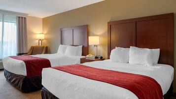 Habitación de hotel con dos camas, cada una con ropa de cama blanca y mantas rojas. Dos mesitas de noche con lámparas, una silla y una ventana con cortinas.