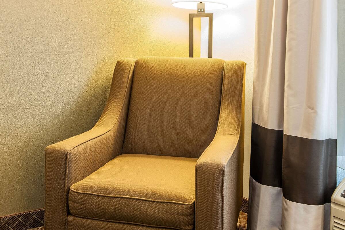 A tan armchair in a room with a lamp and curtains.
