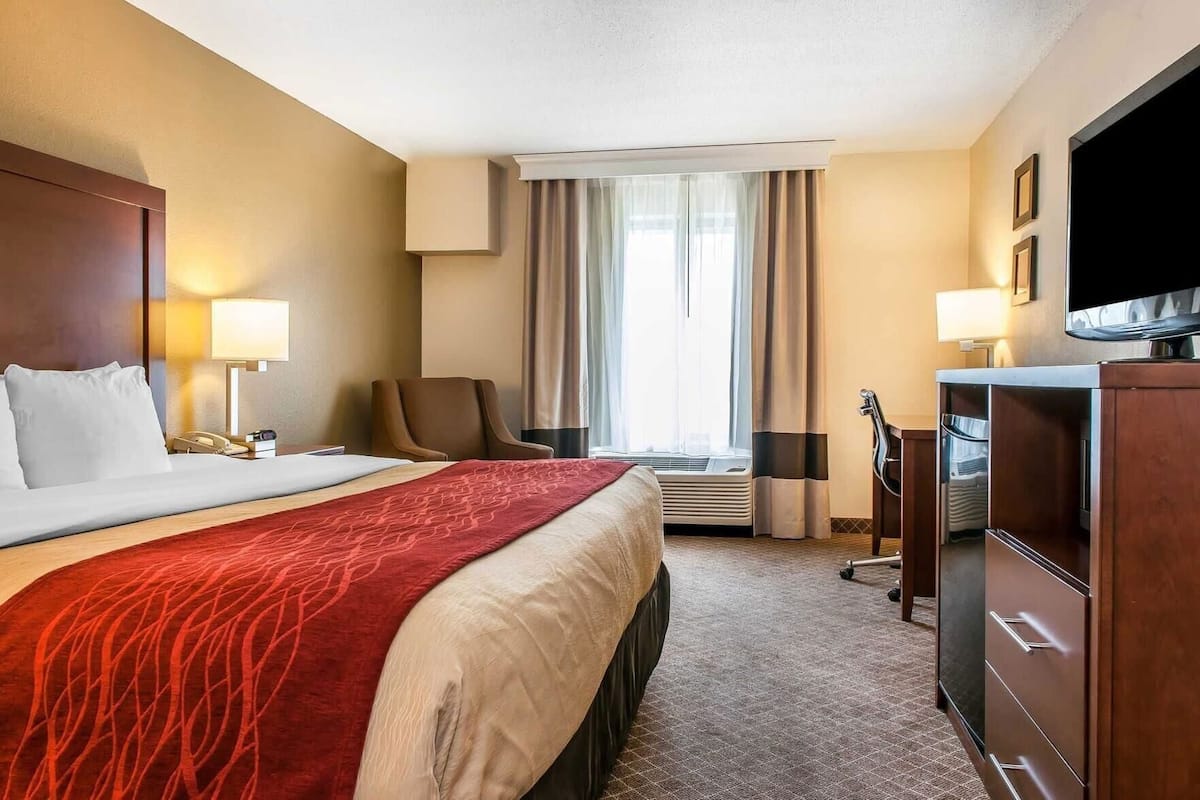 A hotel room with a bed, a desk, a chair, a television, and a window with curtains.