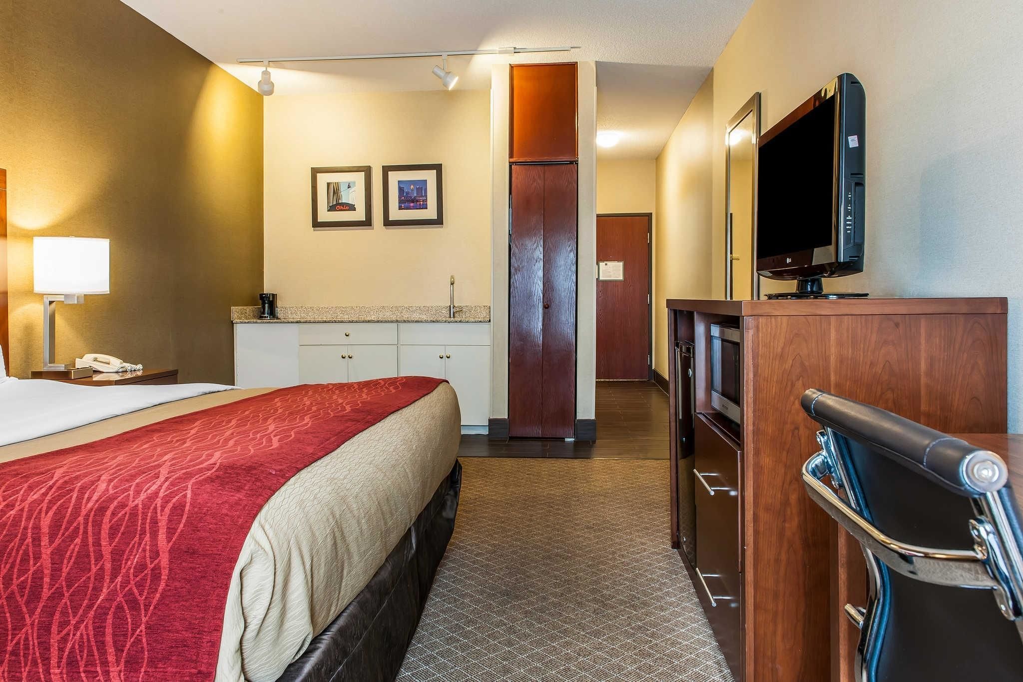 A hotel room with a bed, a desk, a television, a minibar, and a bathroom door.