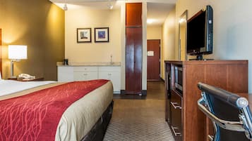 A hotel room with a bed, a desk, a television, a minibar, and a bathroom door.