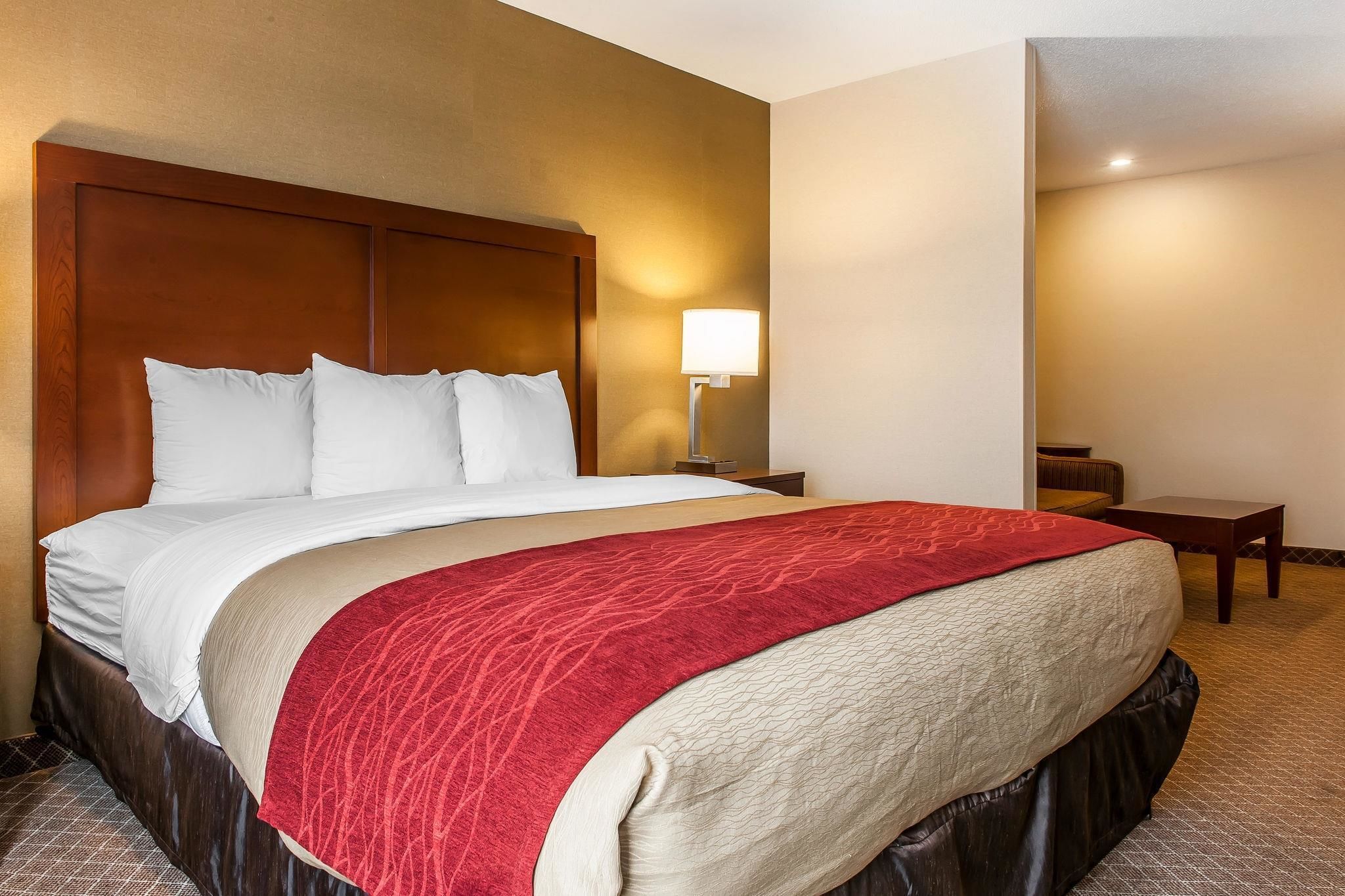 A hotel room with a large bed, a nightstand, a lamp, and a small table.