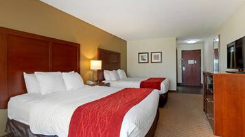 Quarto de hotel com duas camas, uma escrivaninha, uma lâmpada, uma televisão e uma porta que dá para outro cômodo.