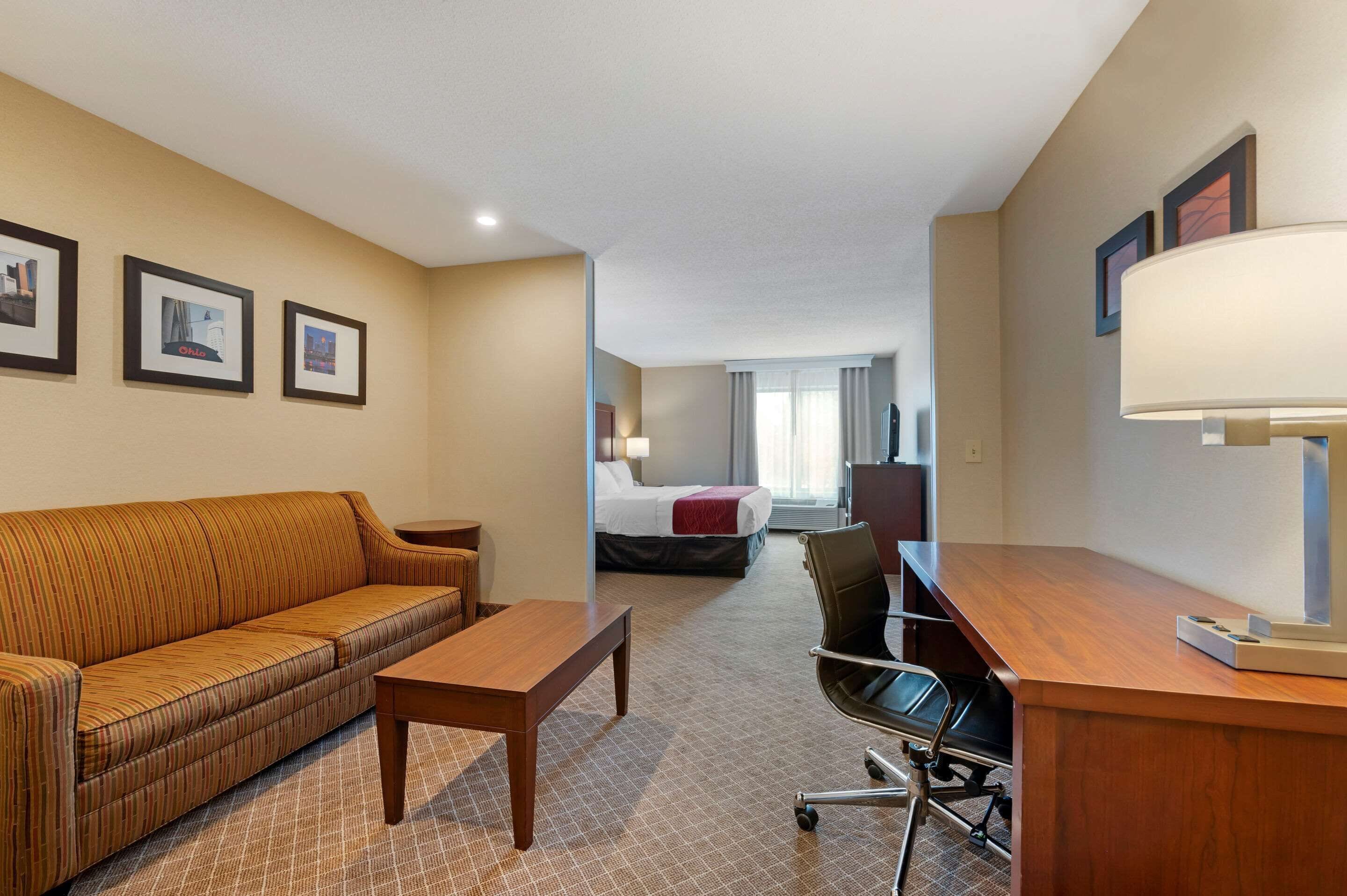 A hotel room with a sofa, a desk, a chair, a bed, and a lamp.