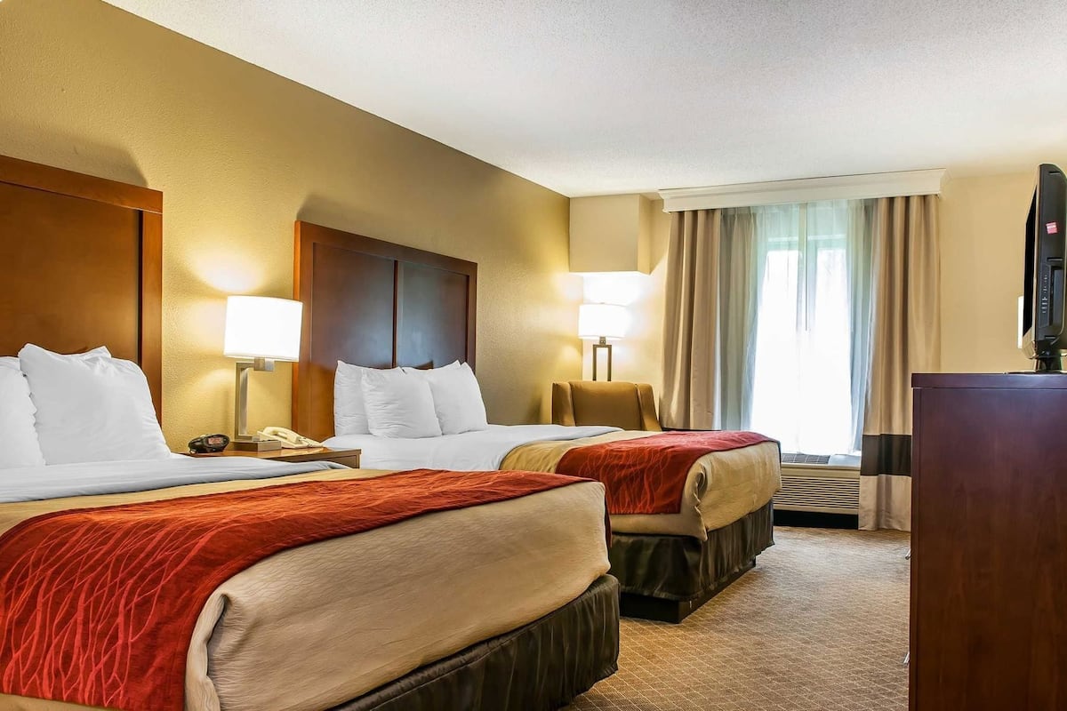 A hotel room with two beds, a TV, a desk, and a window with curtains.