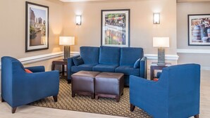 A modern living room with a blue sofa set, two side chairs, and a matching ottoman. There are framed pictures on the walls and two floor lamps. - Comfort Inn near Frost Bank Center (San Antonio)