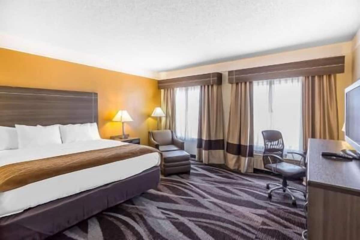 Een hotelkamer met een bed, twee stoelen, een bureau, een televisie en gordijnen.