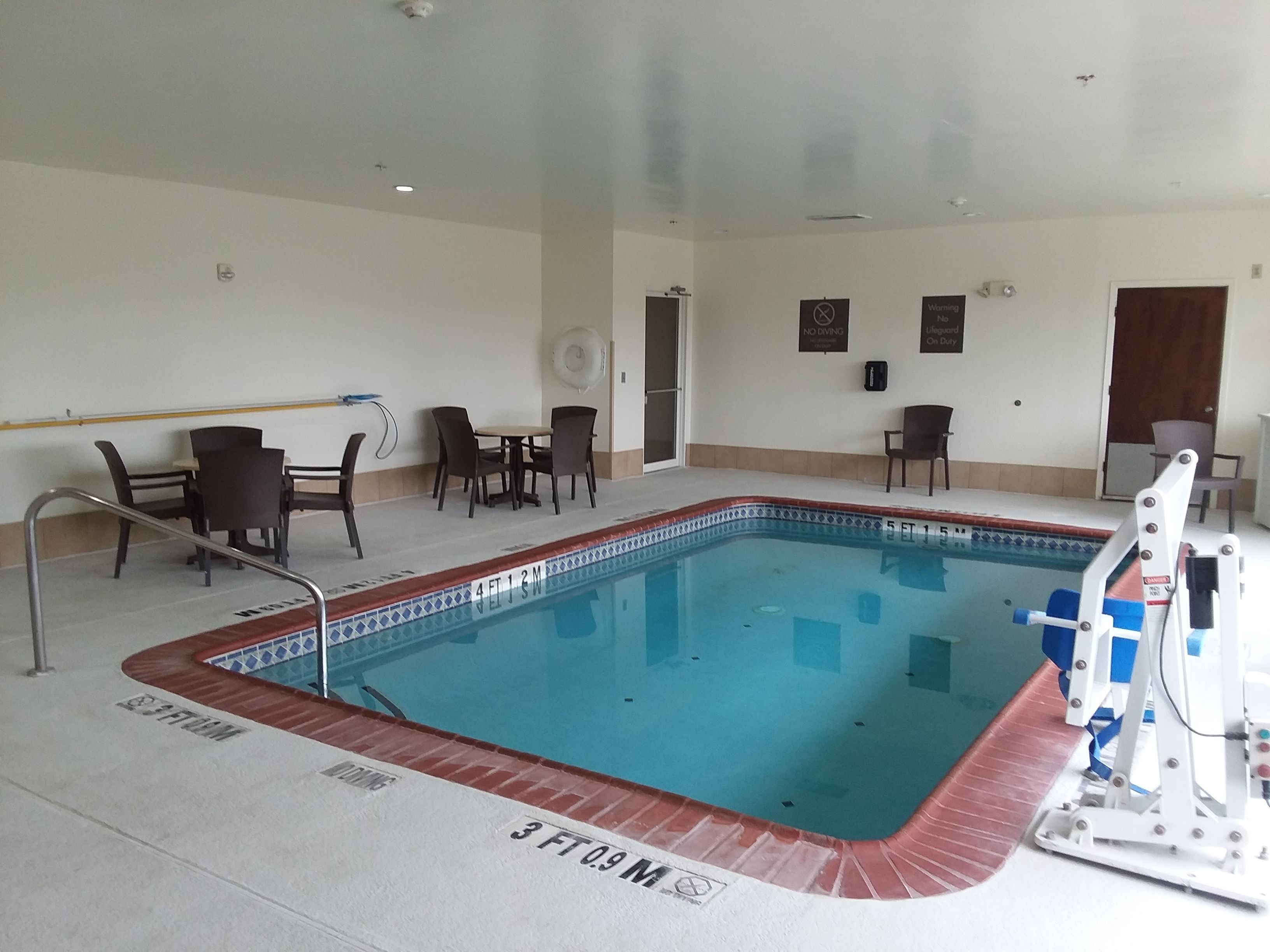 An indoor swimming pool with a tiled edge, a lifeguard chair, and a pool ladder.