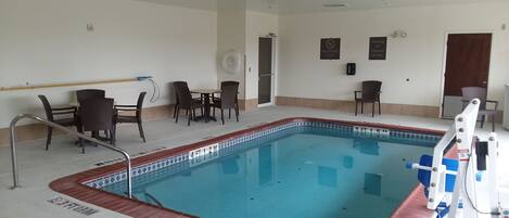 Una piscina interior con borde de azulejos, una silla de socorrista y una escalera de piscina.