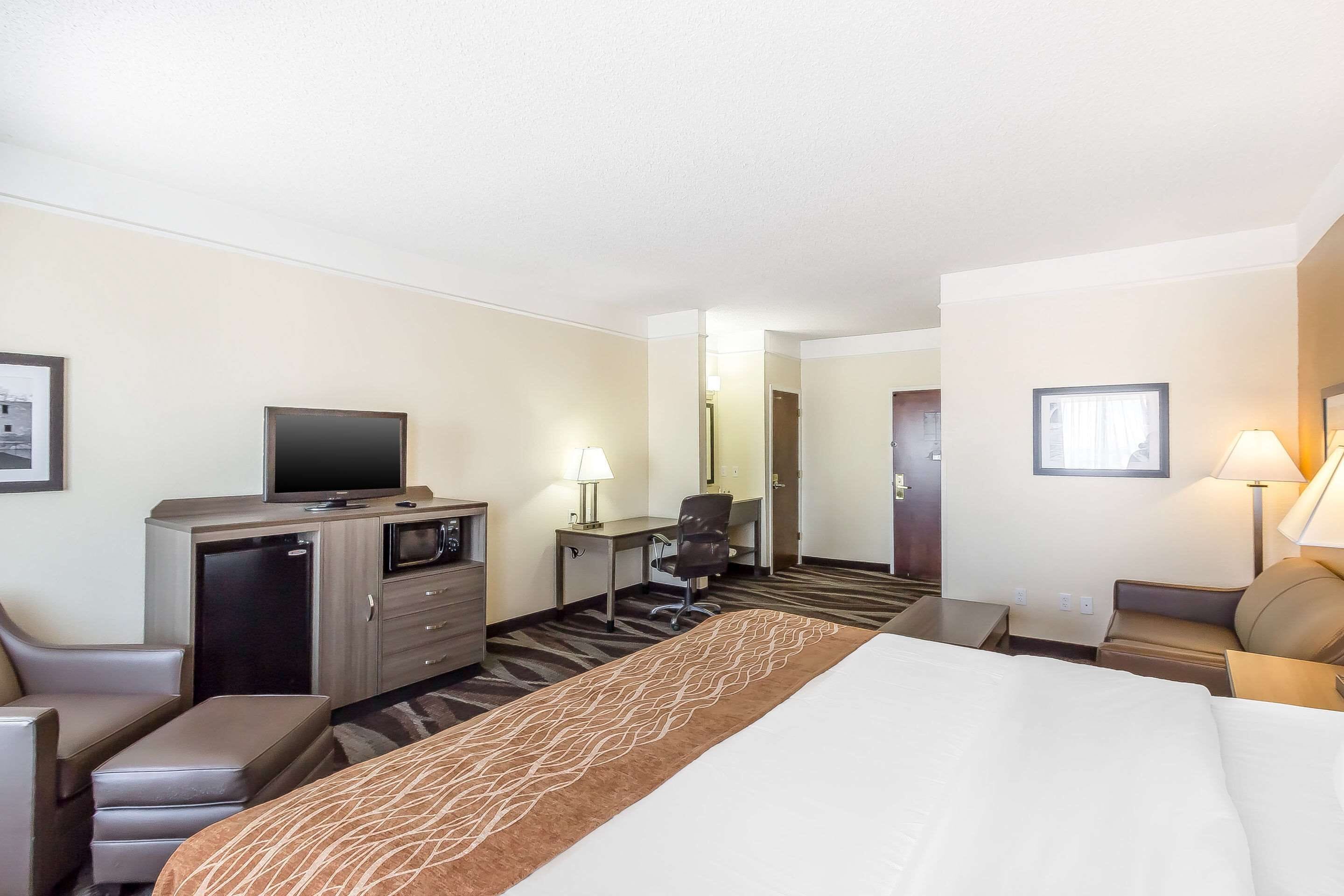 A hotel room with a bed, a desk with a chair, a television, a desk lamp, a microwave, and a refrigerator.
