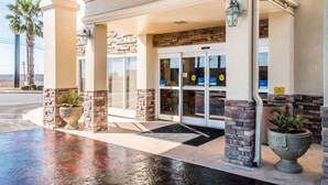 A hotel entrance with a stone facade, glass doors, and a palm tree in the background. - Comfort Inn near Frost Bank Center (San Antonio)
