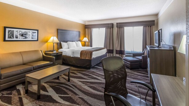A hotel room with a bed, a sofa, a desk, a chair, a TV, and a window with curtains. - Comfort Inn near Frost Bank Center (San Antonio)