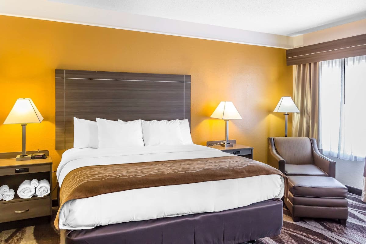 Een hotelkamer met een groot bed, twee nachtkastjes met lampen, een stoel en een raam met gordijnen.