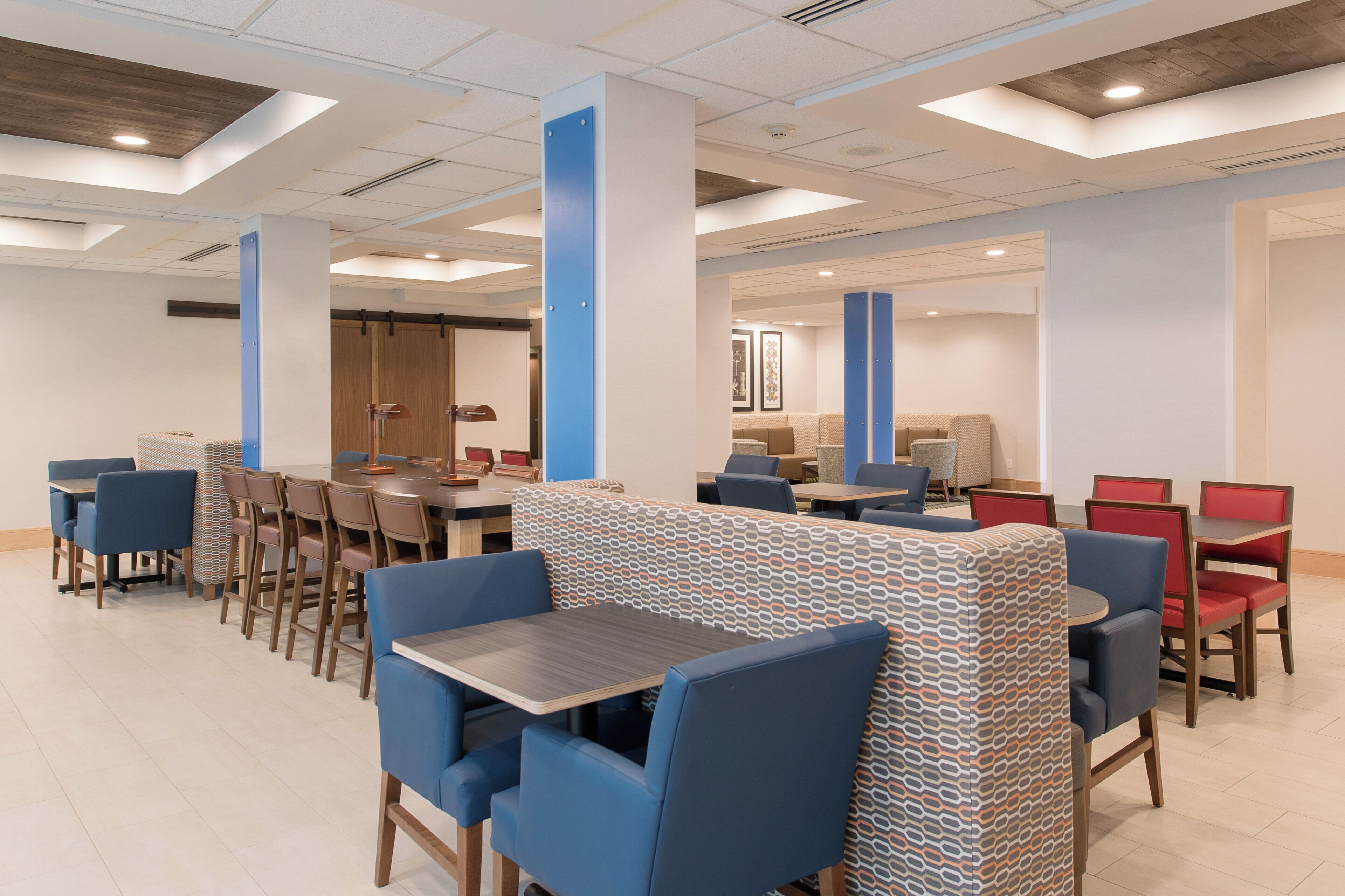 Un moderno vestíbulo de hotel con una larga mesa común, zonas de estar individuales y una recepción.