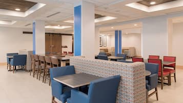 Un moderno vestíbulo de hotel con una larga mesa común, zonas de estar individuales y una recepción.