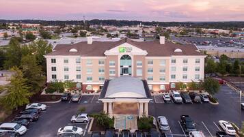 A hotel with a central entrance, multiple parking spaces, and a view of the surrounding area.