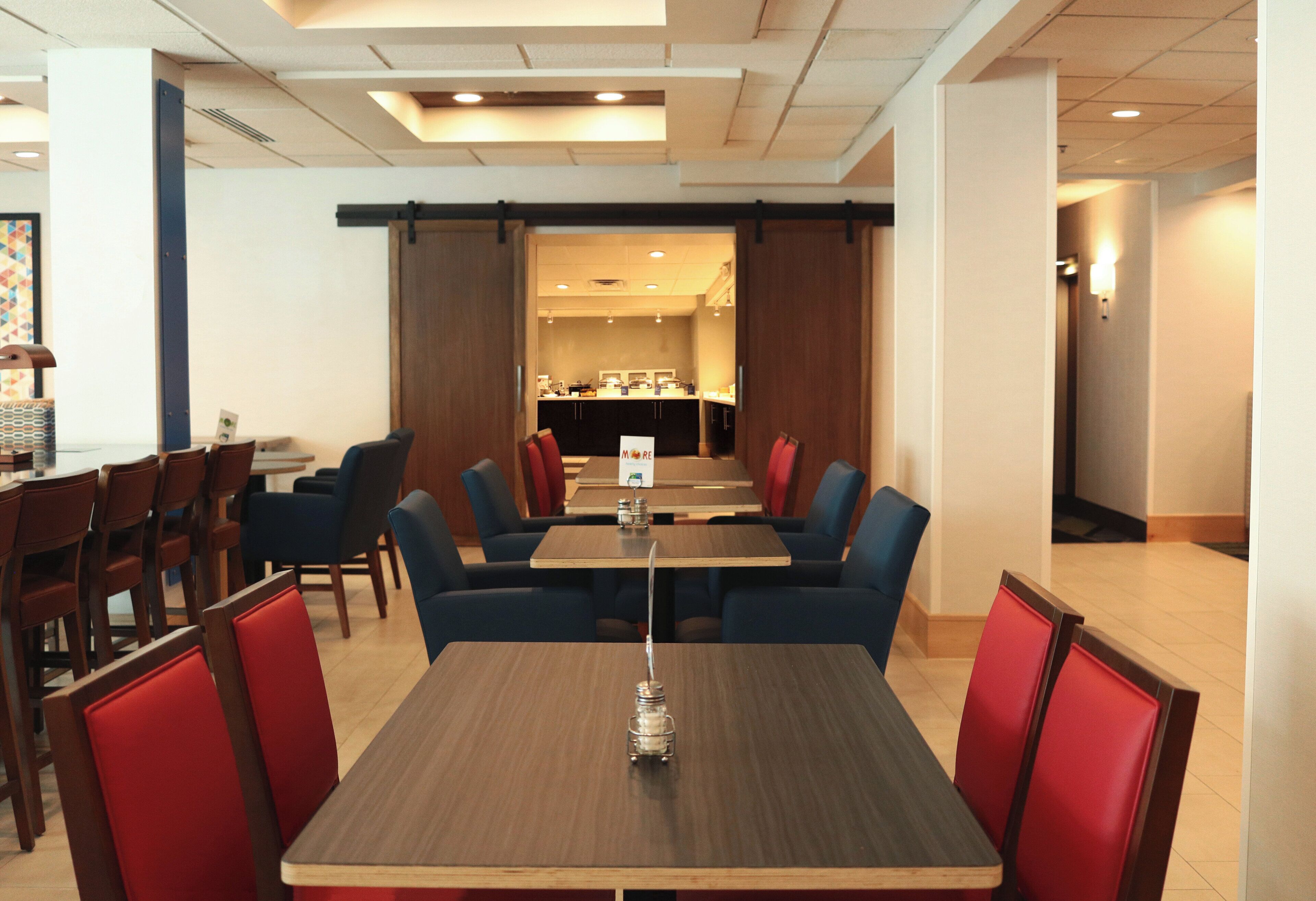 Un restaurante con mesas y cabinas, una barra y vistas al área de cocina.