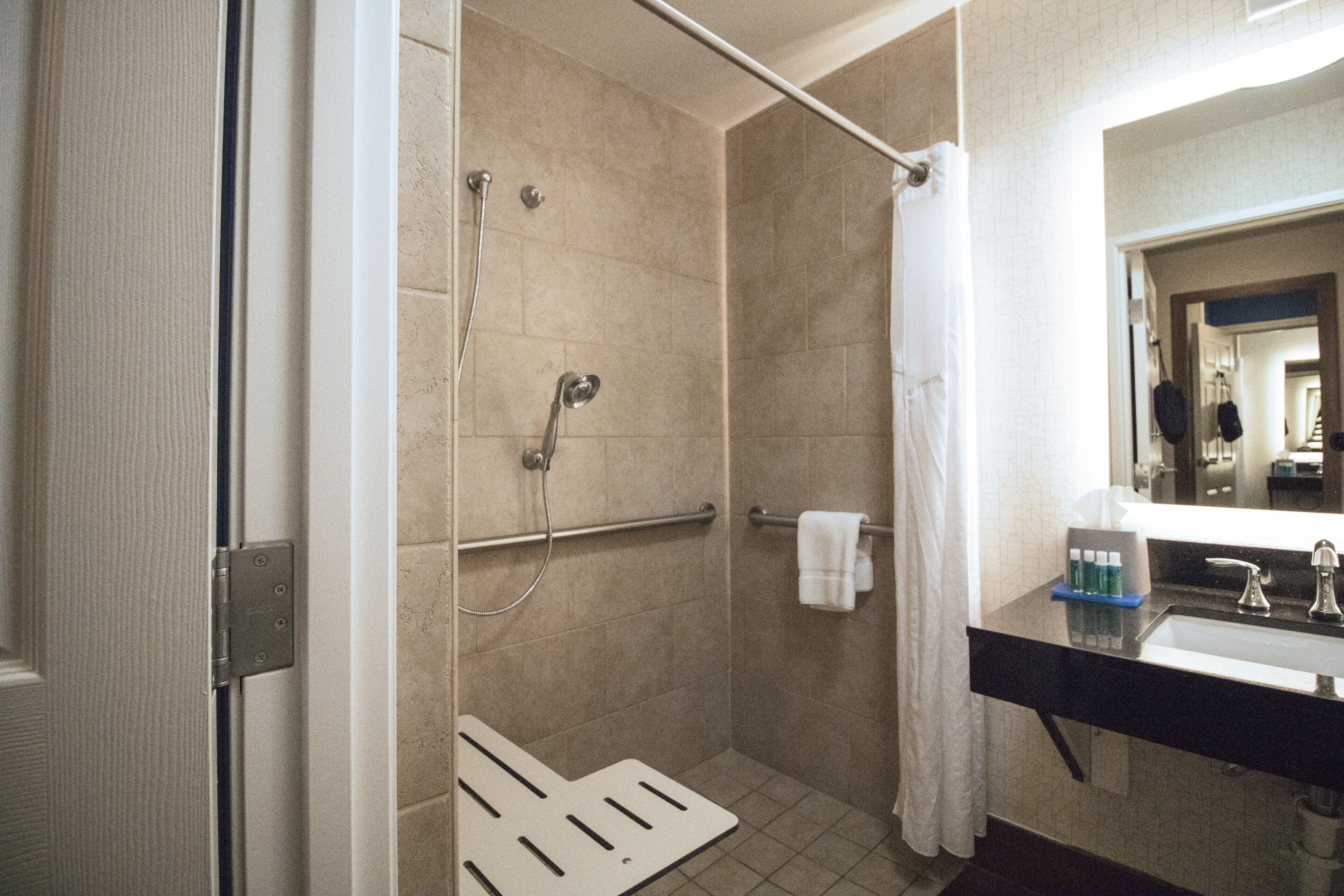 A hotel bathroom with a shower, a toilet, and a sink with a mirror.