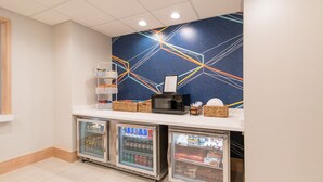 Un espace d’accueil comprenant un comptoir, deux distributeurs de boissons, un four à micro-ondes et un mur décoratif.