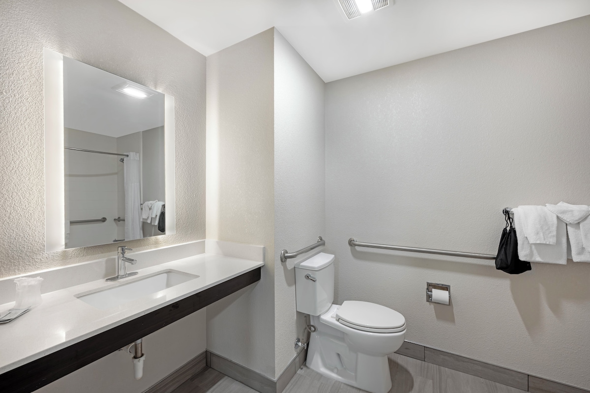 A modern bathroom with a large mirror, a white sink, a toilet, and a towel rack.