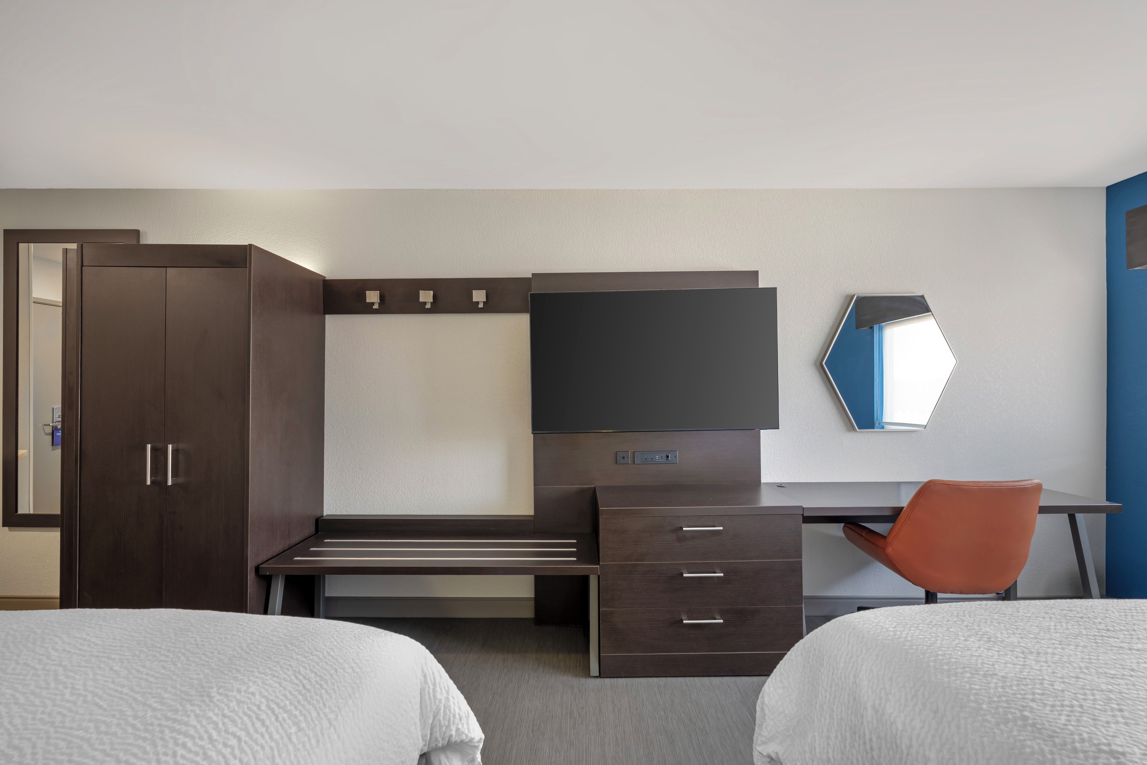 Una habitación de hotel con cama, escritorio, silla, armario y televisor.