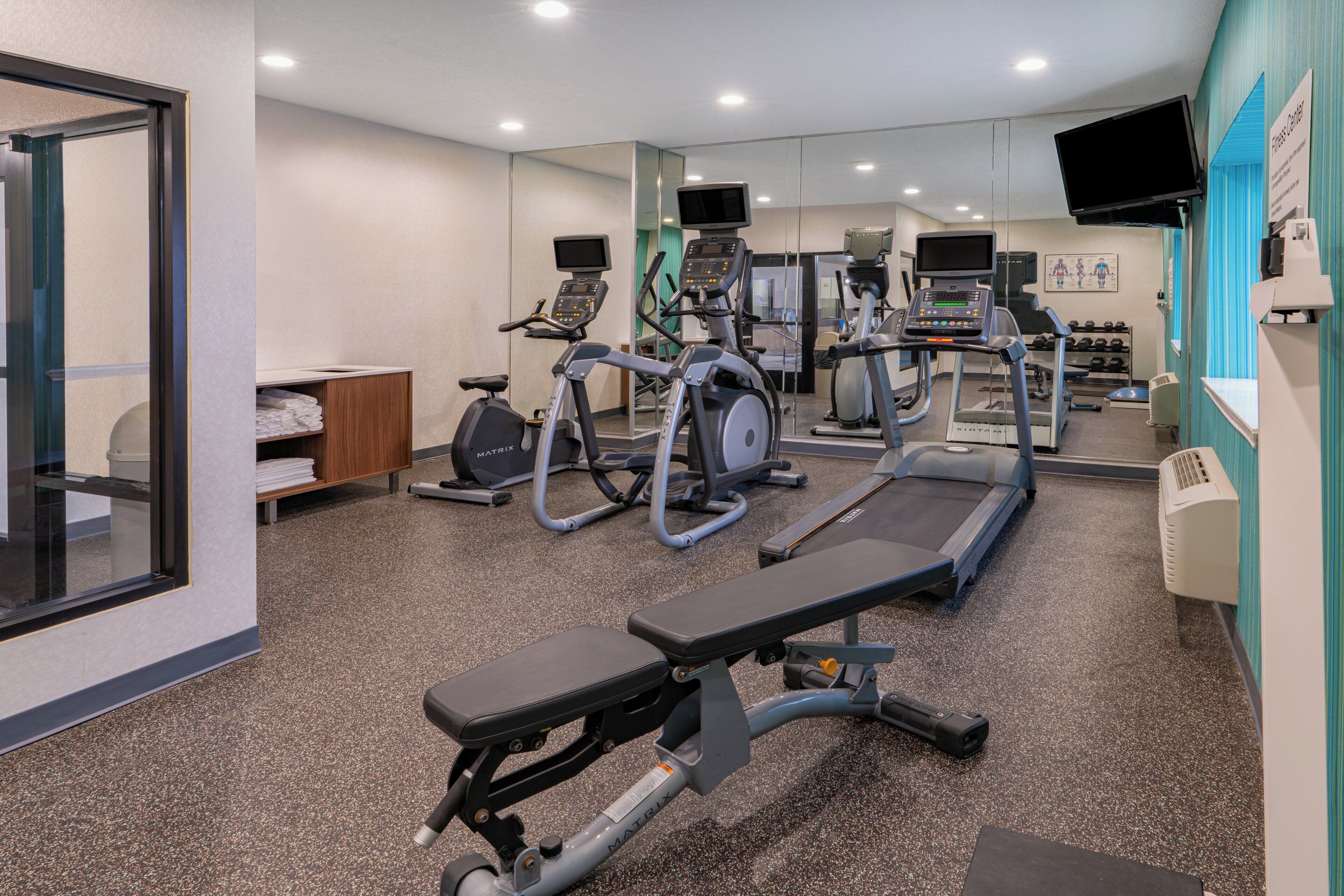 Een sportschool met loopbanden, elliptische trainers en een bank.