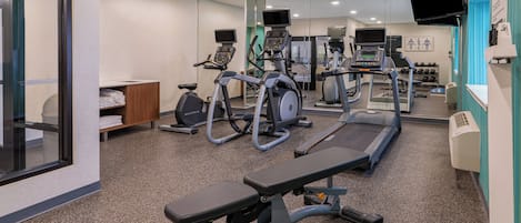 Un gimnasio con cintas de correr, elípticas y un banco.