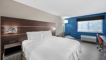 A hotel room with a large bed, a desk, a chair, a window, and a wall-mounted lamp.