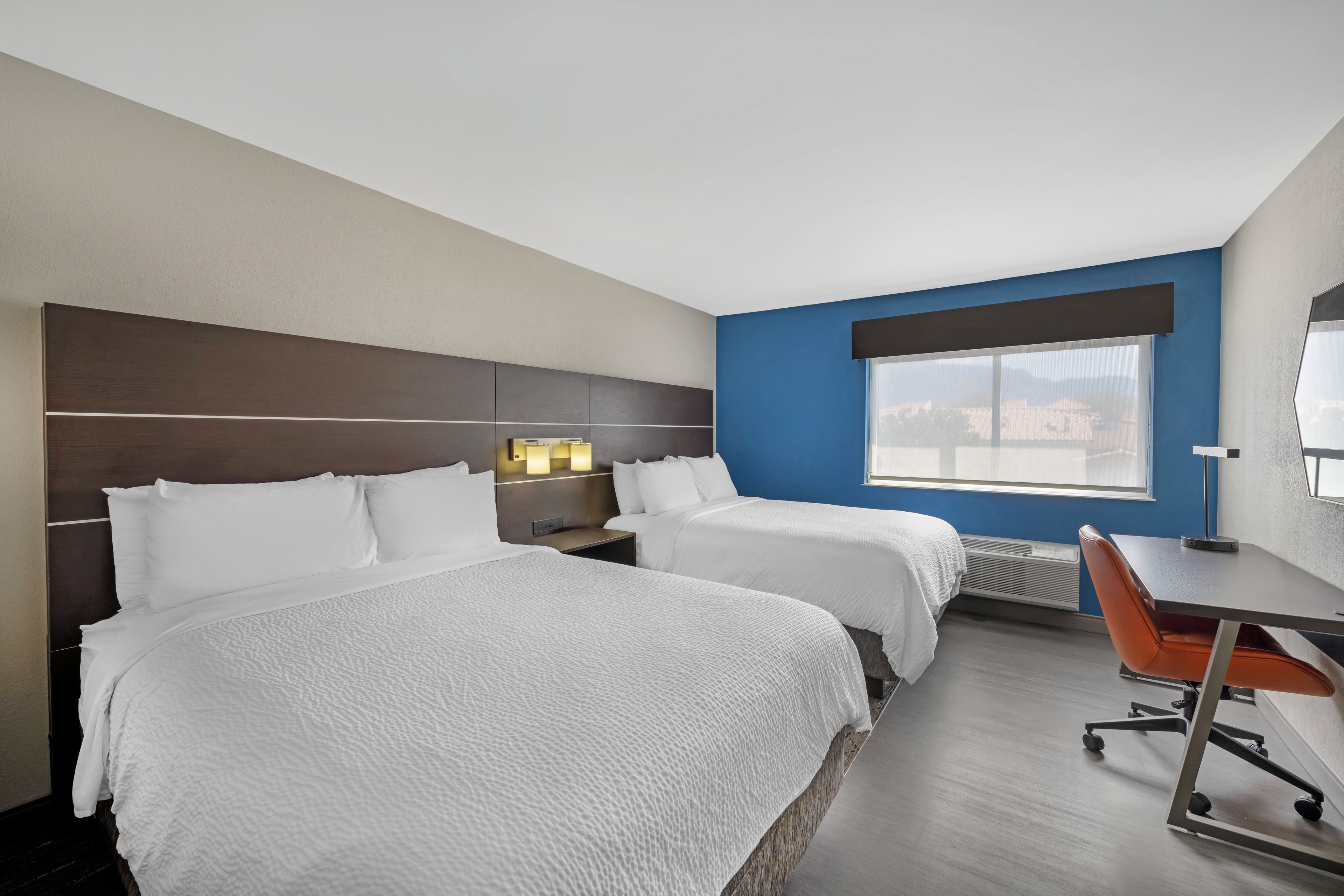 A hotel room with two beds, a desk, and a chair.