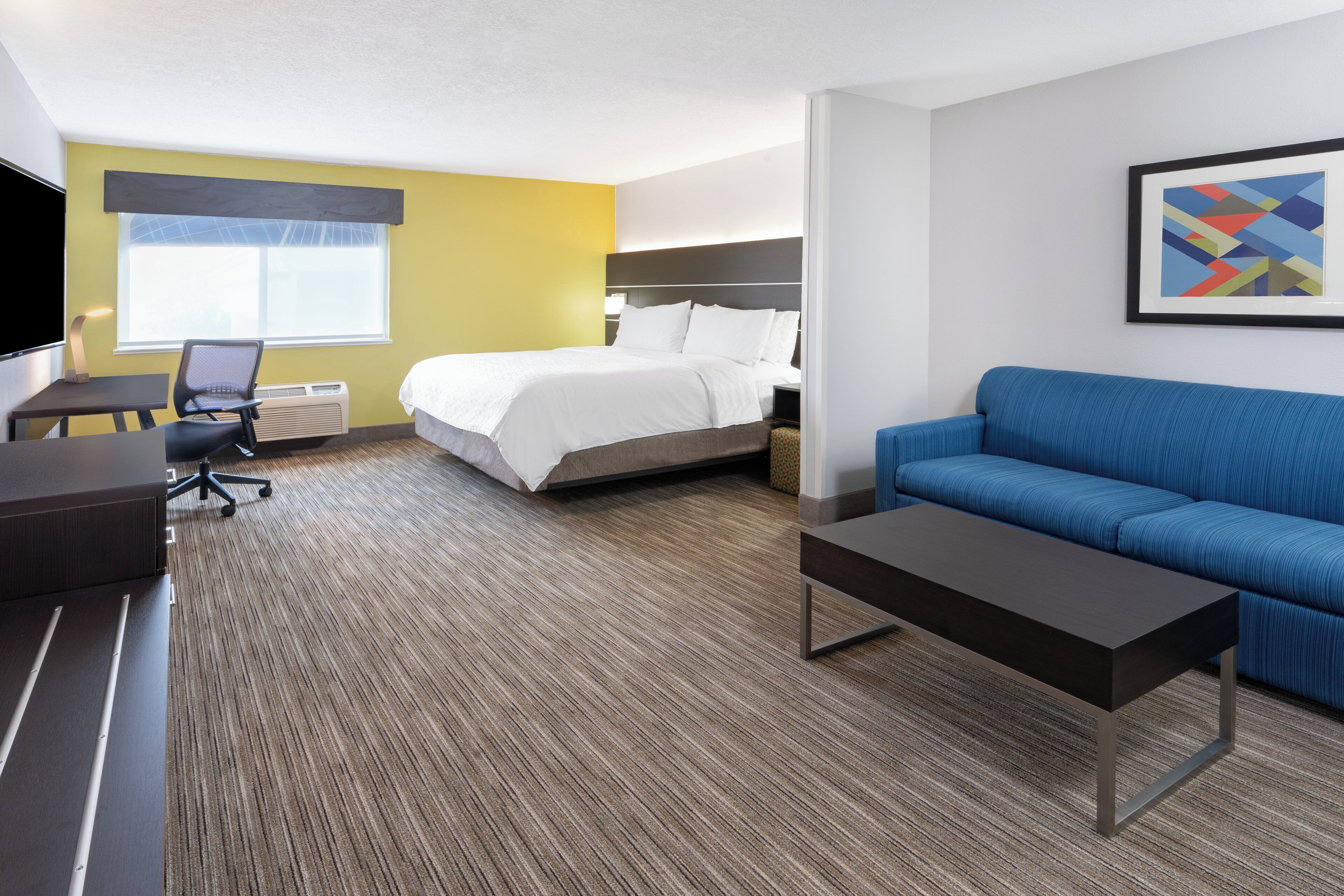A hotel room with a bed, a blue sofa, a desk with a chair, and a TV.