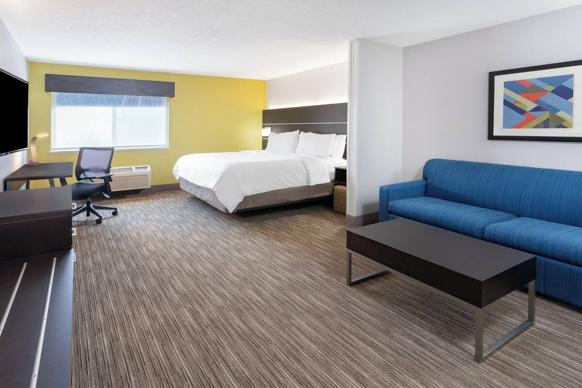 Une chambre d’hôtel avec un lit, un canapé bleu, un bureau avec une chaise et une télévision.