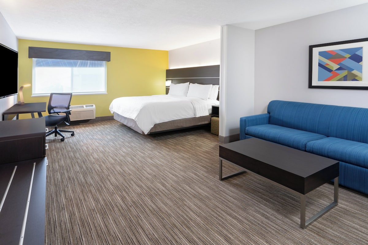 A hotel room with a bed, a blue sofa, a desk with a chair, and a TV.