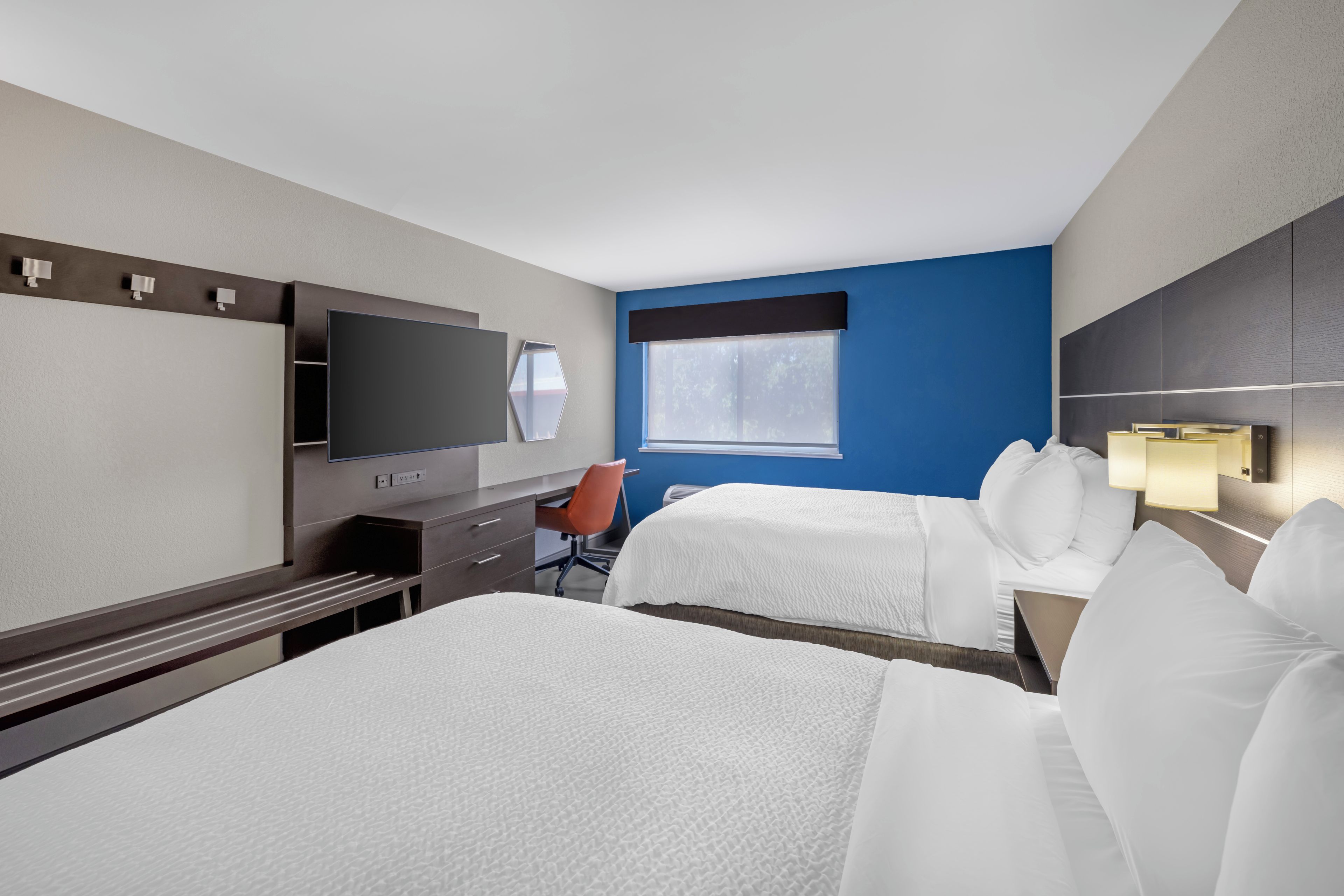 A hotel room with two beds, a desk, a chair, a television, and a window.